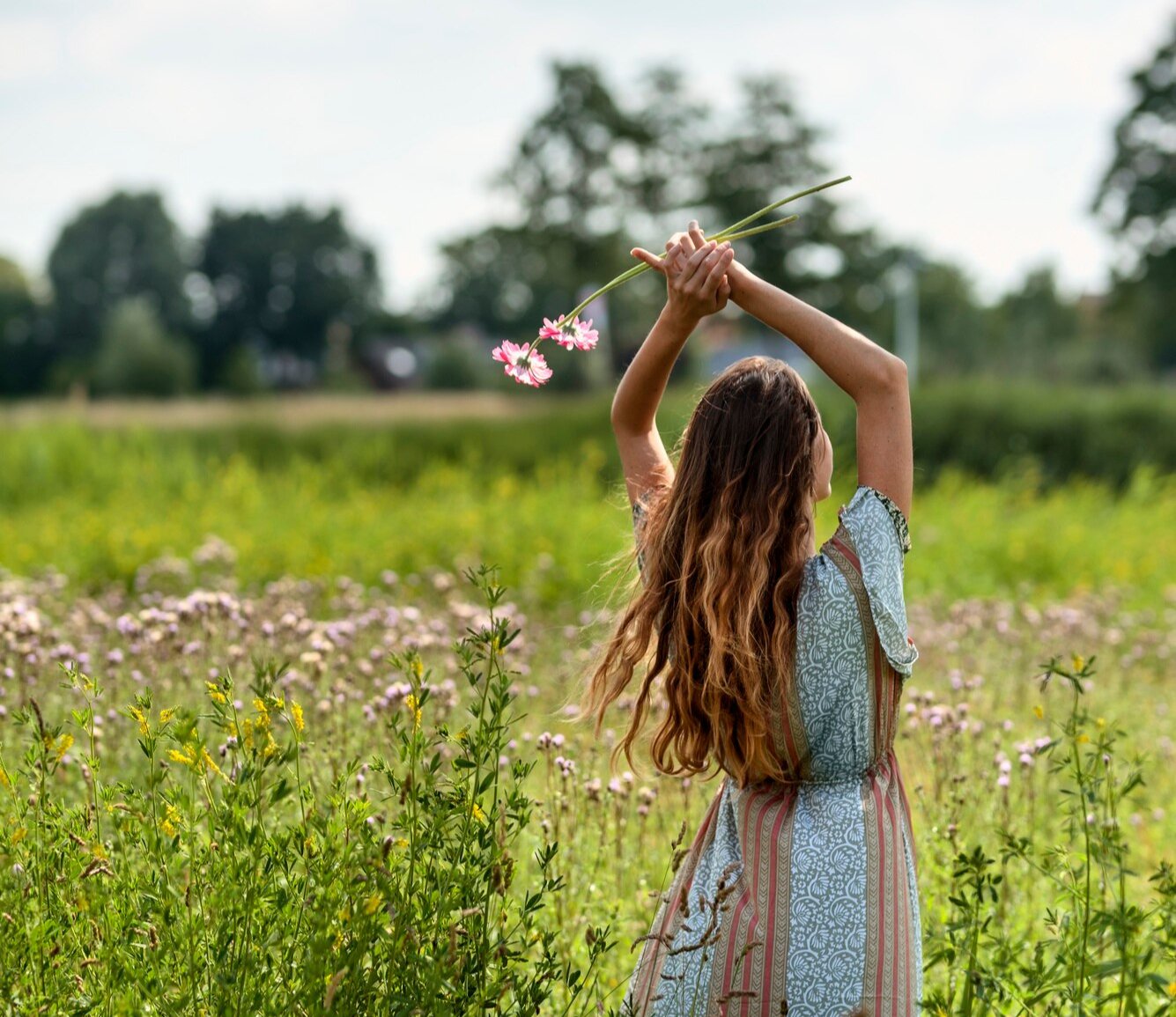 mujer caminando entre flores con los brazos en alto